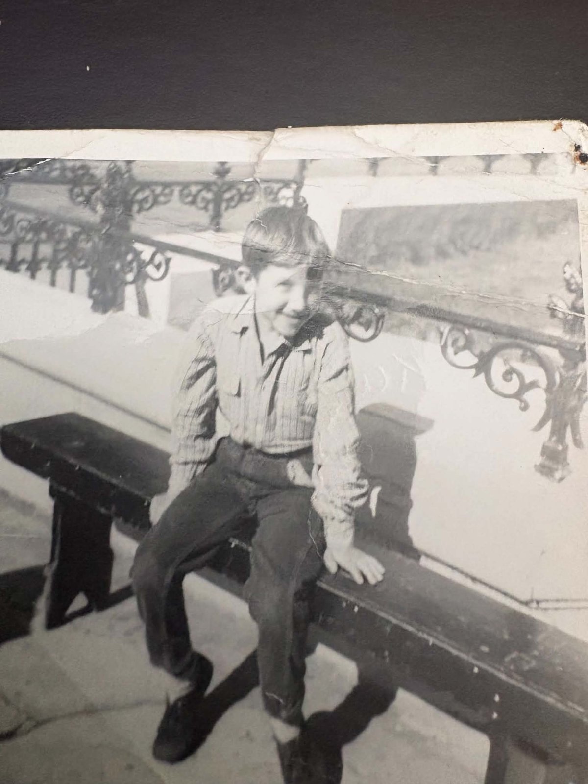 A boy sitting on a bench — the original, damaged photograph